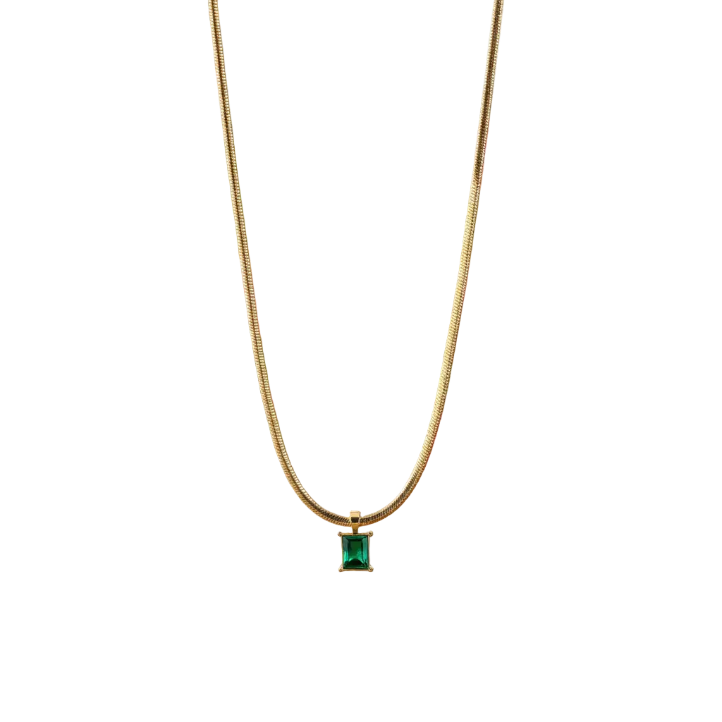 Gold necklace with a green gemstone pendant on a wooden surface with a blurred floral background
