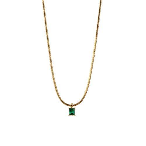 Load image 1 in gallery view. Gold necklace with a green gemstone pendant on a wooden surface with a blurred floral background