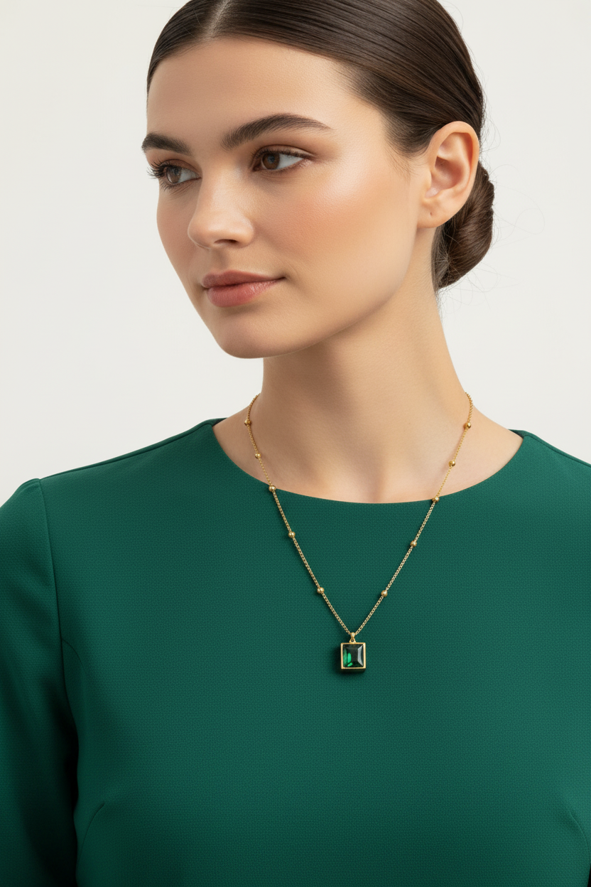 Woman wearing a gold necklace with a green pendant on a plain background